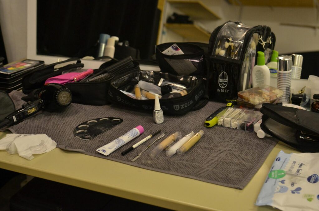 From above of hair dryer and cosmetic bags with various makeup supplies and products placed on table in dressing room